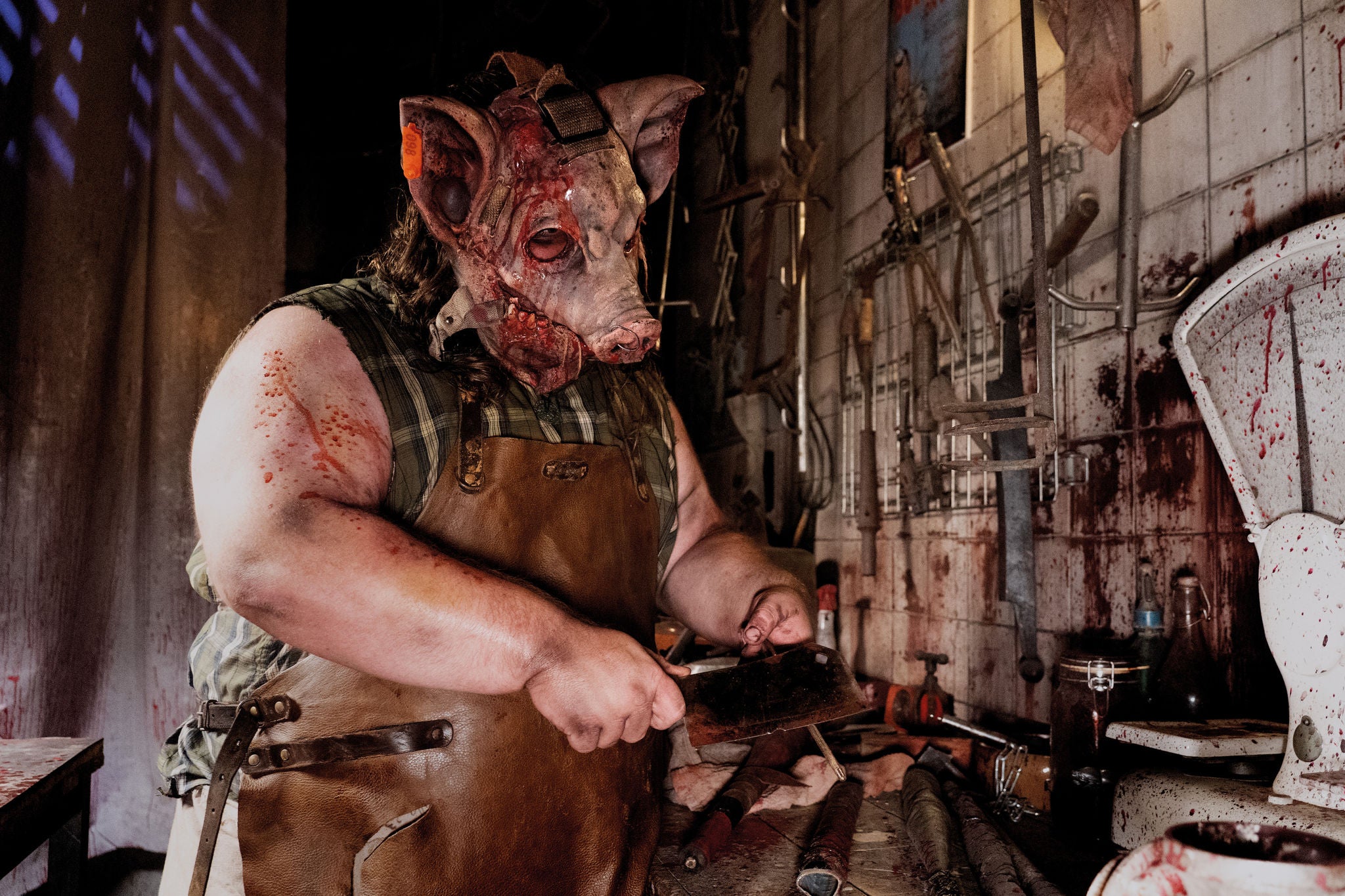 A monster with a pig head is cutting meat with bloody butcher's knives 